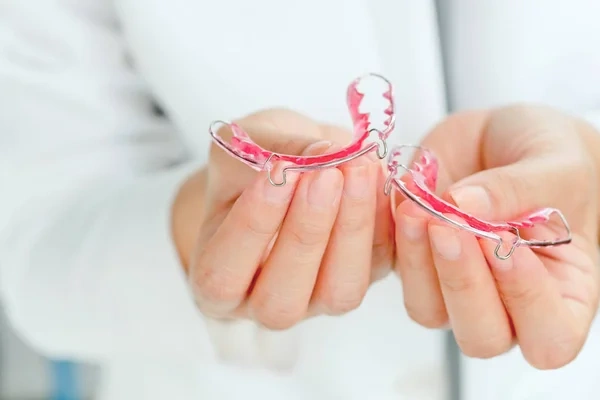 A dental professional in a white coat holding a pair of pink removable Hawley retainers.