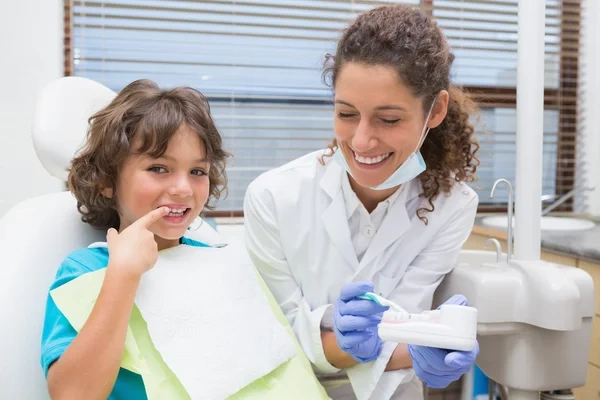 A dentist demonstrating tooth-brushing techniques to a smiling child patient during a dental checkup