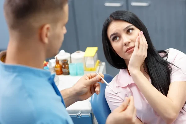 A dentist looking at a girl with her hand on her cheek, showcasing signs of tooth pain