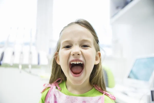 A happy young girl opening her mouth wide to show her healthy primary teeth during a pediatric dental checkup