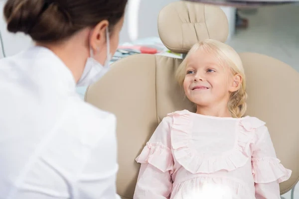 A smiling young girl sitting comfortably in a dental chair while consulting with a pediatric dentist.