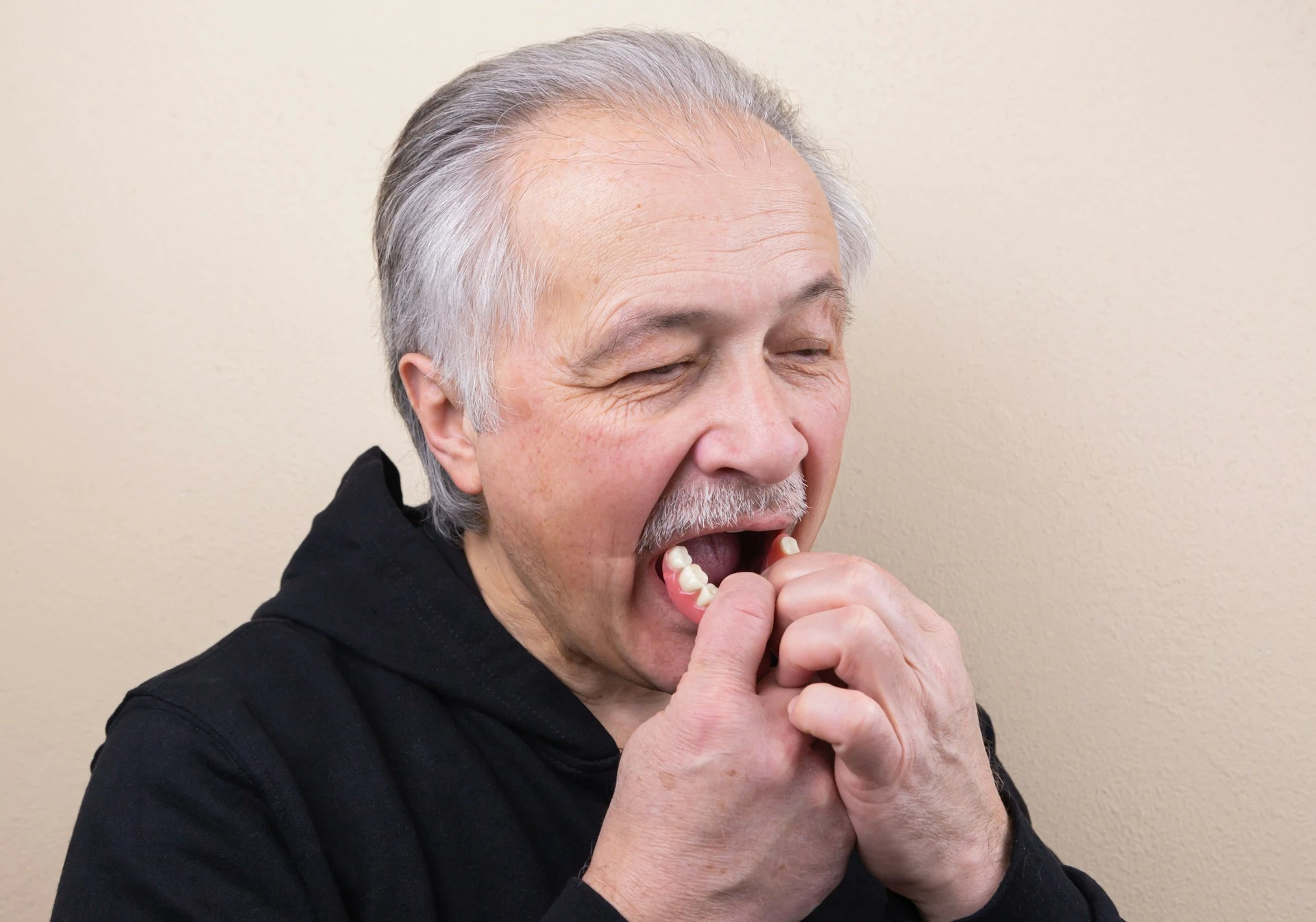 An old gray-haired man puts on his denture.