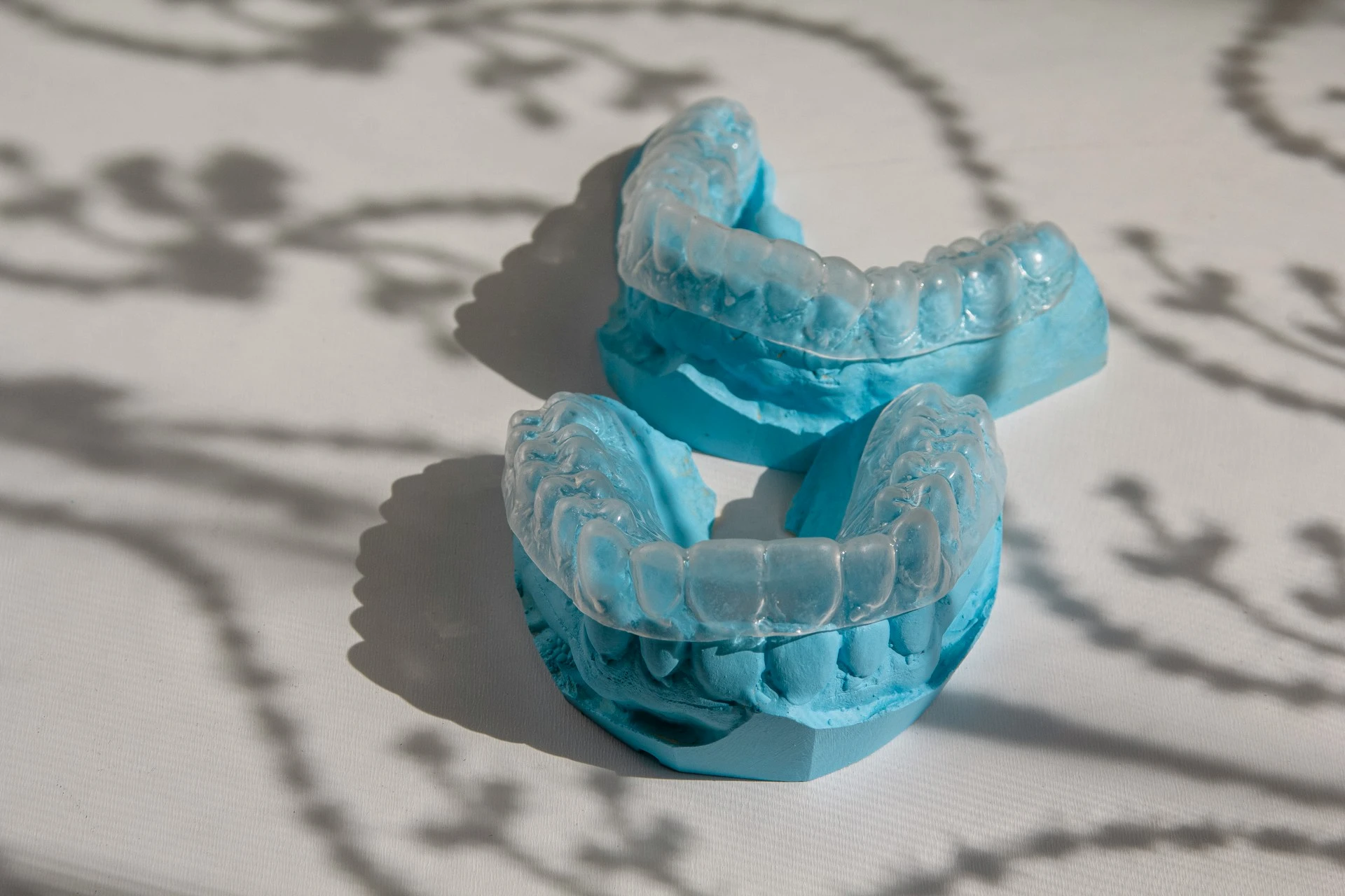 Clear Invisalign aligner trays fitted onto blue dental plaster cast models of teeth.