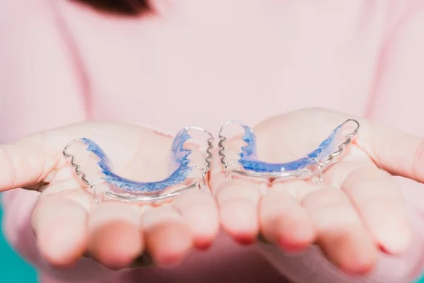 Close-up of a patient holding a pair of blue acrylic and wire Hawley retainers in her open hands.