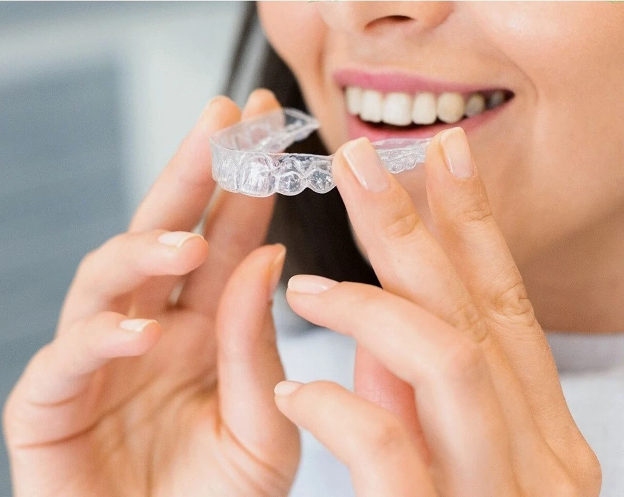 Close-up of a smiling woman holding a clear Invisalign aligner tray near her teeth