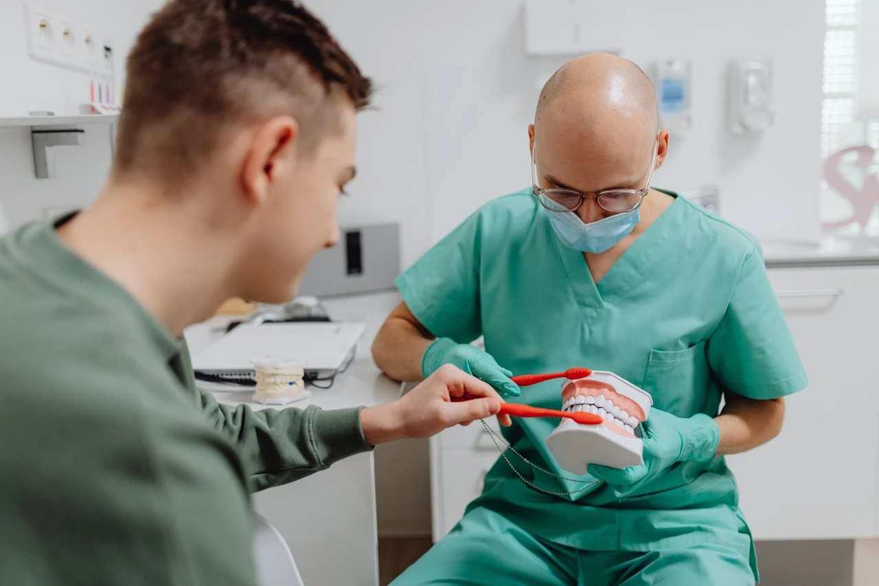 Dentist demonstrating proper brushing technique to patient using dental model