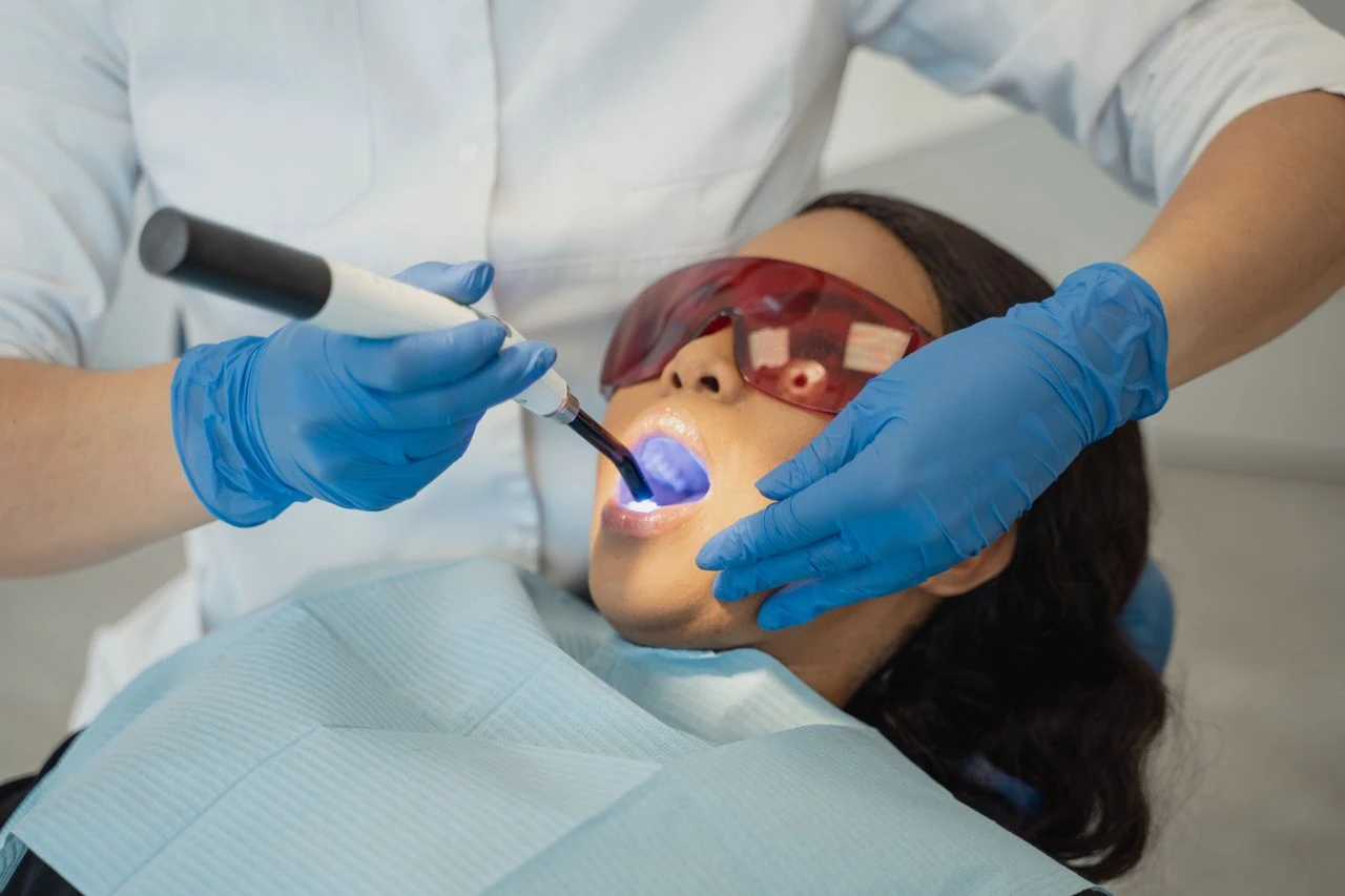 Dentist performing dental treatment using curing light on patient wearing protective eyewear