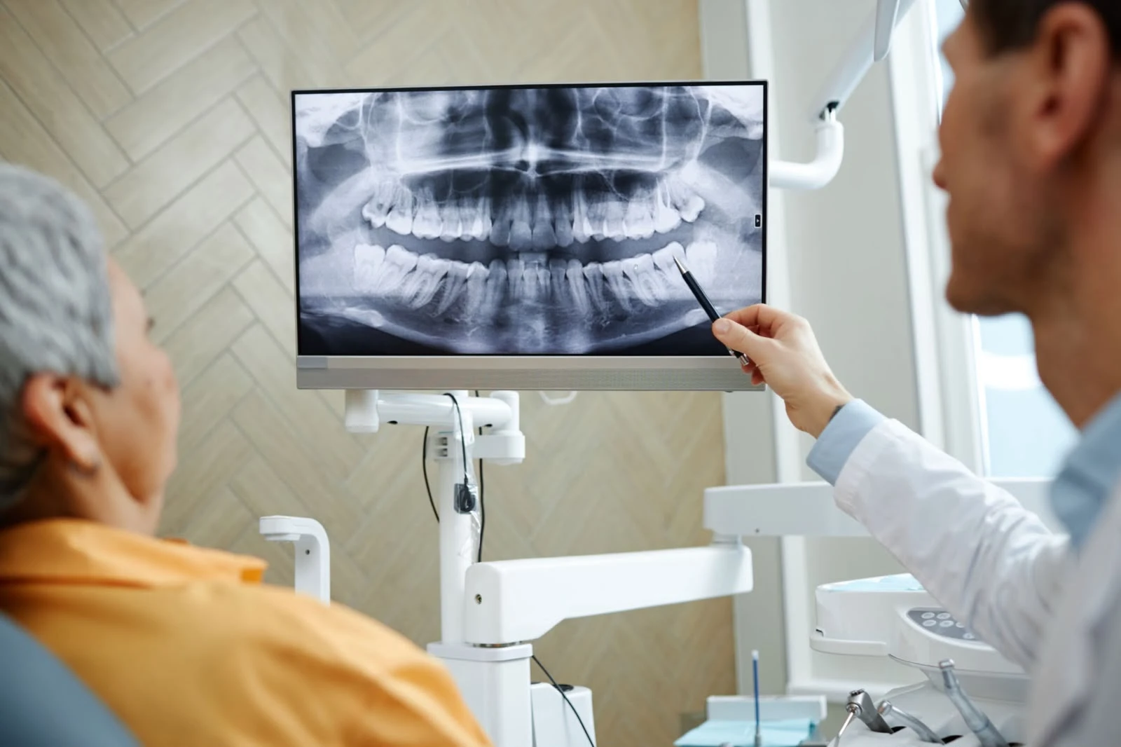 Dentist pointing to a panoramic dental X-ray during an oral surgery diagnostic examination.