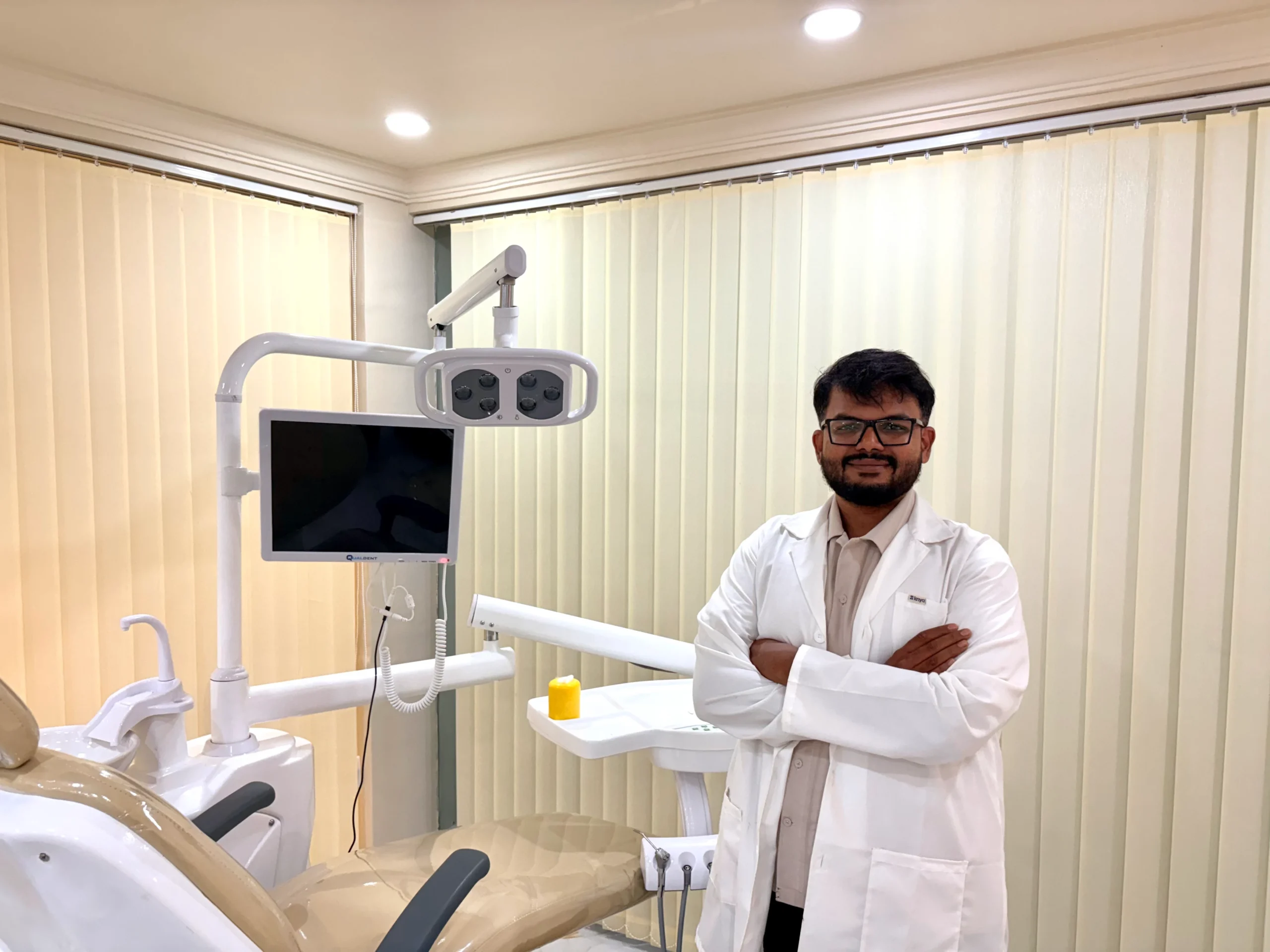 Dr. Rahmathullah standing with folded arms in front of a modern dental chair setup at Unique Dental clinic.