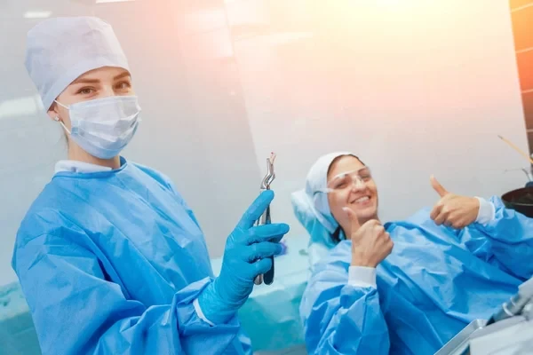 Oral surgeon holding extraction forceps with a removed tooth next to a smiling patient.