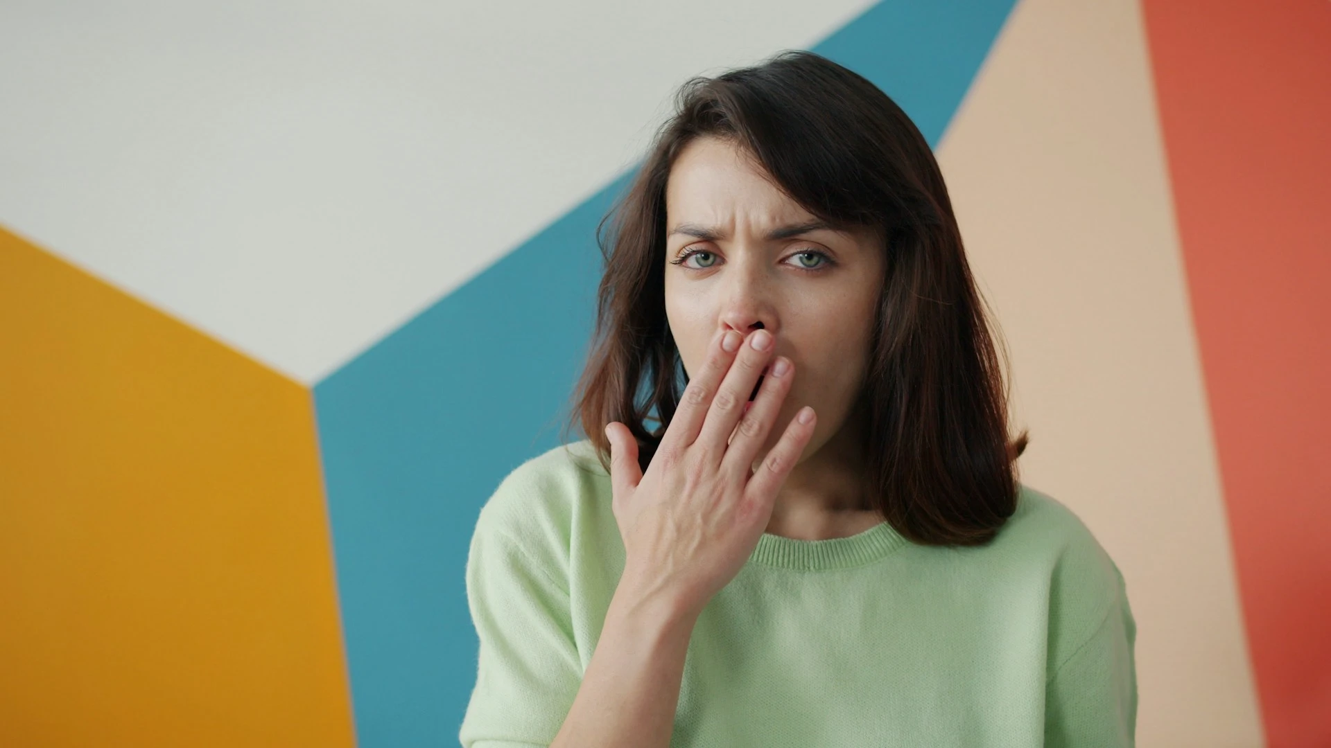 Sleepy woman yawning looking at camera standing on colorful background.
