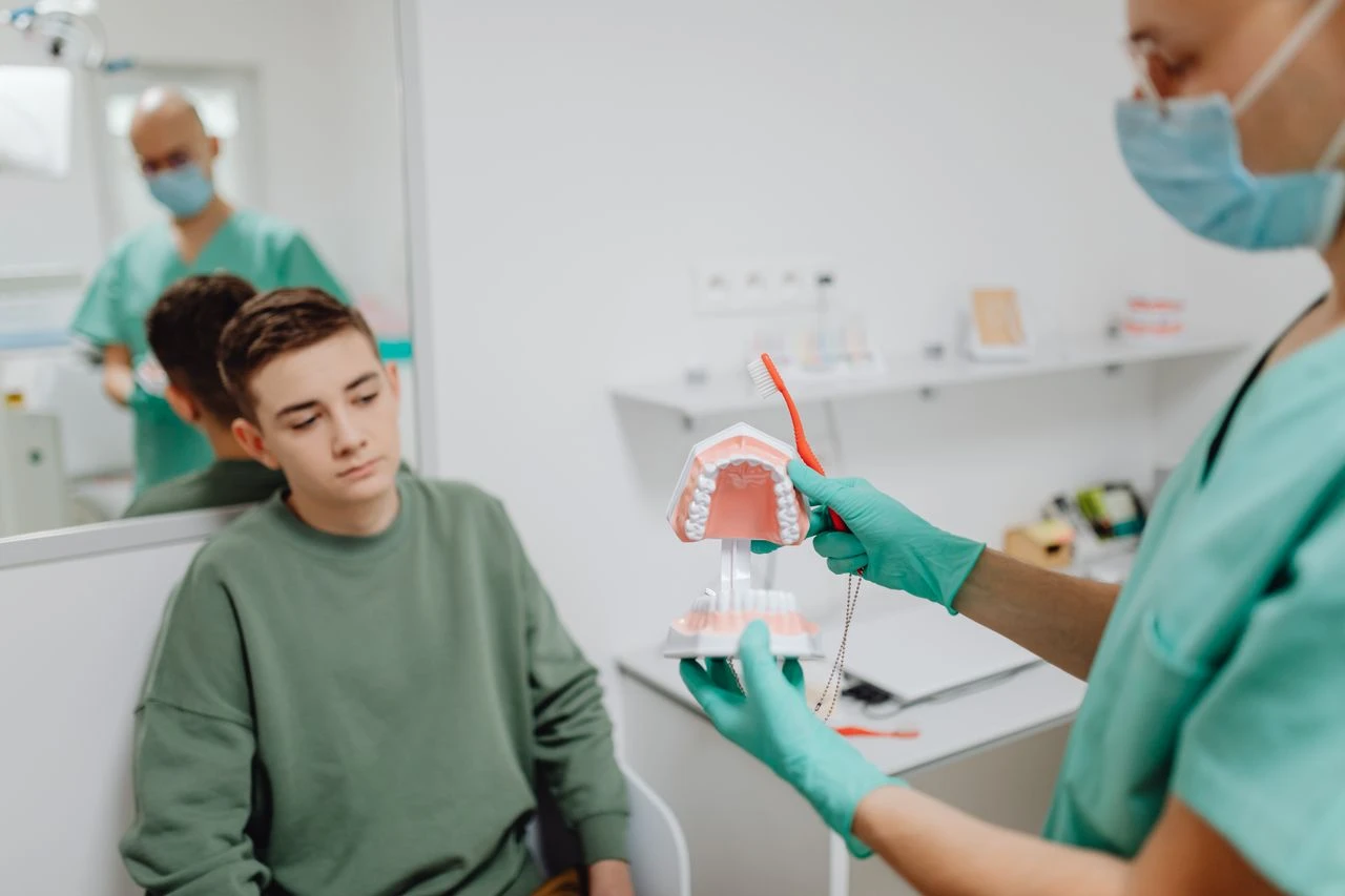 Teenager learning dental hygiene from dentist using a dental model