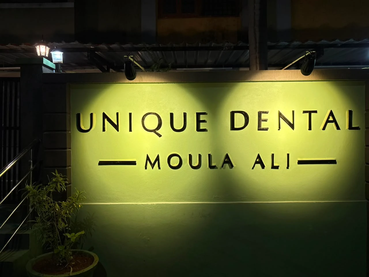 Unique Dental Moula Ali clinic exterior wall signage illuminated at night.